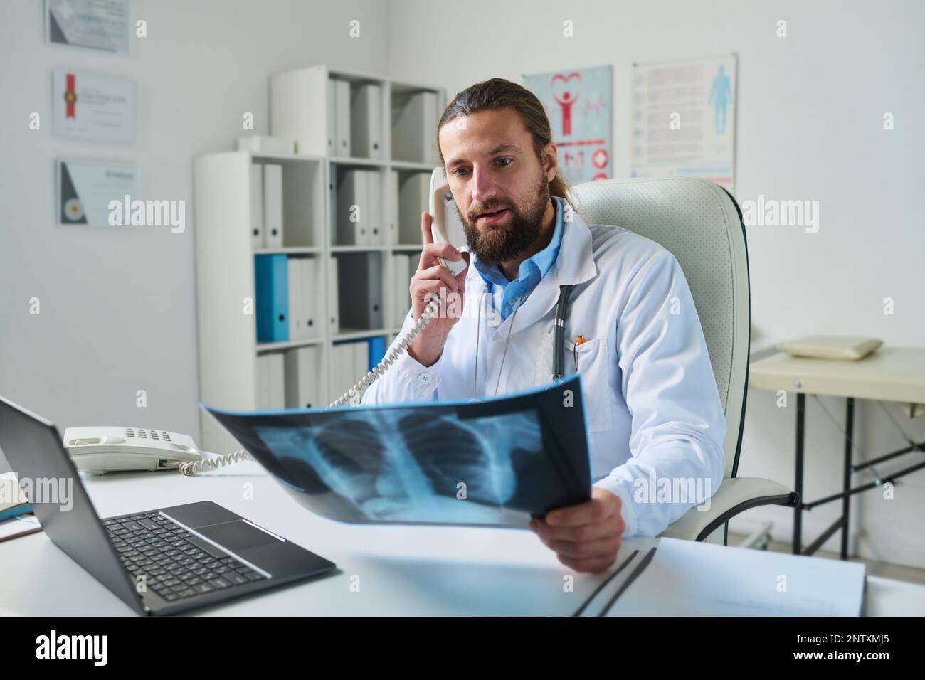 Confident radiologist looking at lung x-ray while sitting by workplace ...