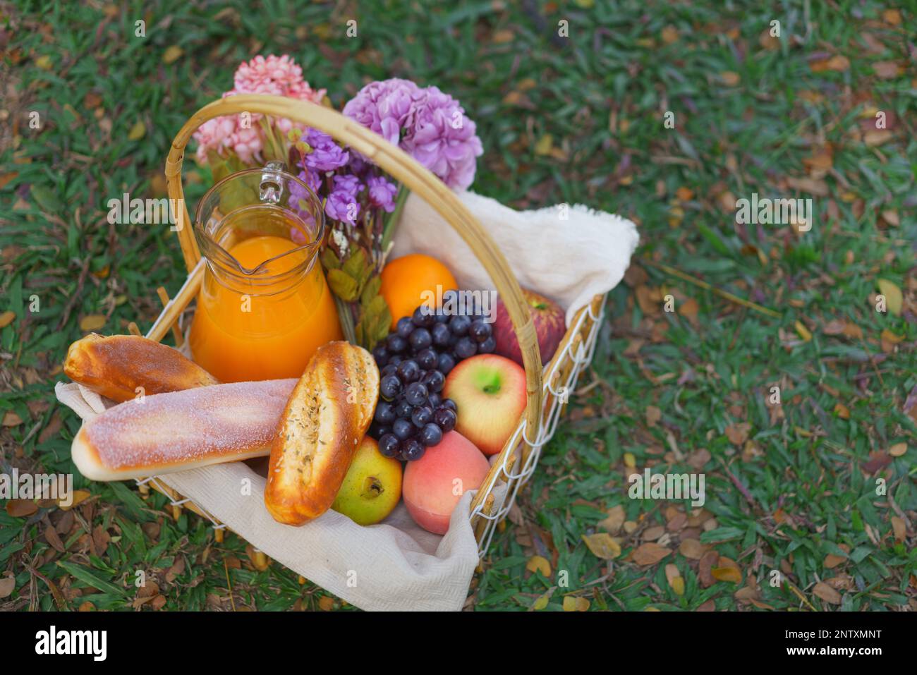 Wicker picnic basket of bakery fruits and orange juice with flowers on ...