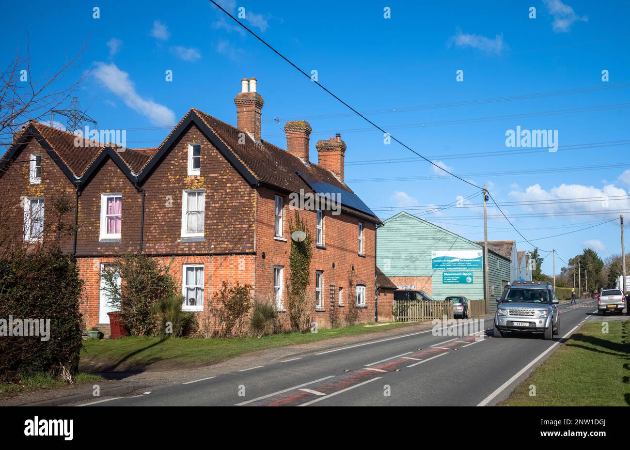 A Land Rover Discovery car drives past some ancient cottages on a country road in Wisborough Green, UK. Stock Photo