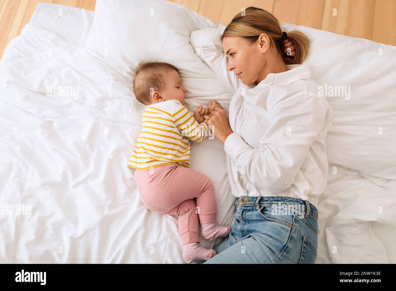 Mother protection. Happy mom lying with her baby girl in bed together ...