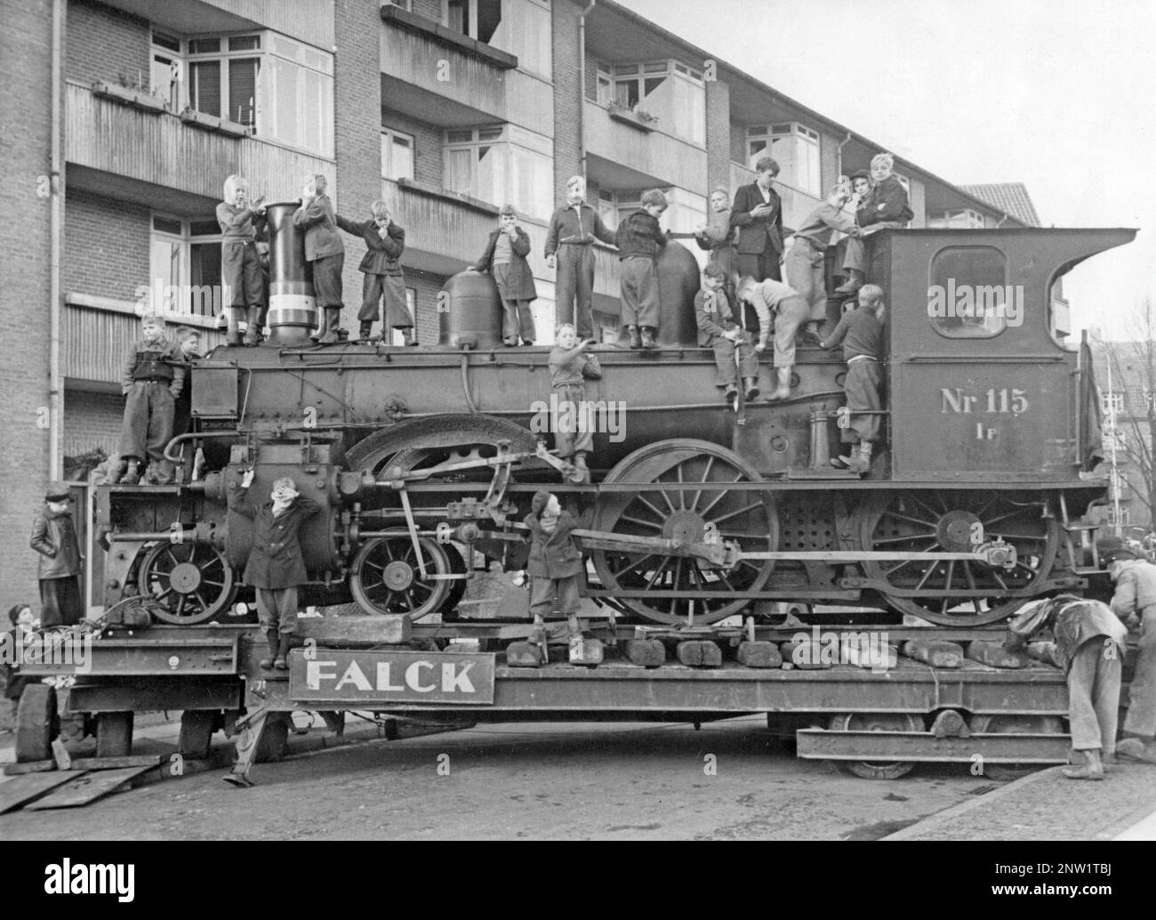 Steam locomotive off the tracks. A group of boys is pictured climbing and being on the locomotive being transported on a narrow street in Stockholm in the 1940s. It is standing on lorrys and looks as if it is being turned in the street, a complicated maneuver. Stock Photo
