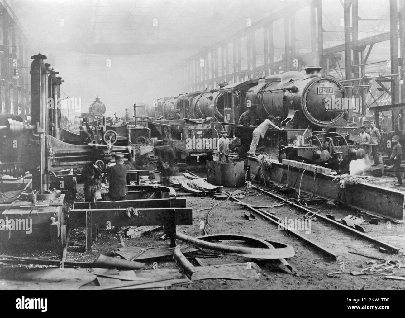 Steam locomotive repair shop Kobe Japan. An interior where several locomotives are seen in a row with mechanics working on them. 1930s Stock Photo