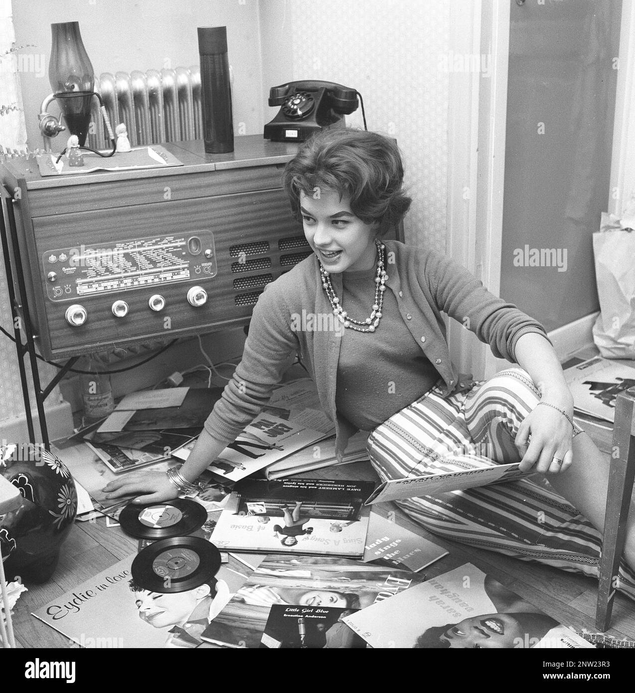 Radio listeners in the past. A woman is seen on the floor with records by popular singers and groups of the 1950s.The combined radio and record player is seen that was a popular item at this time, often a nice piece of furniture in itself, usually in a wooden case. She is swedish singer Lill-Babs Svensson. Sweden 1958 ref BV21-3 Stock Photo