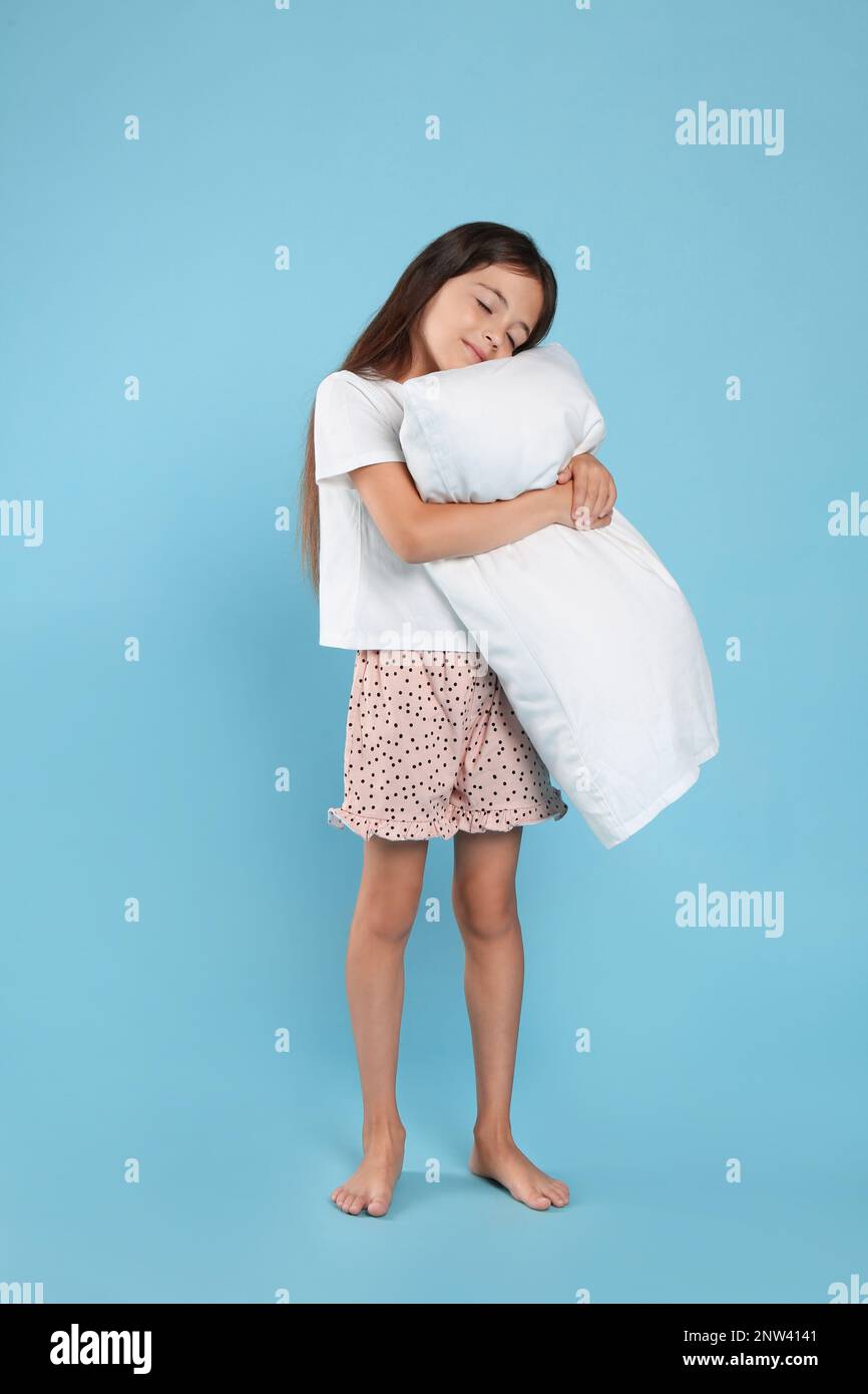 Cute girl wearing pajamas with pillow on light blue background Stock ...