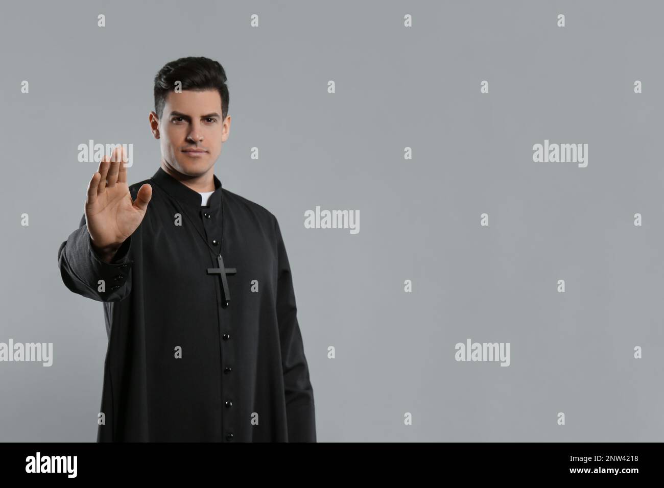 Priest wearing cassock with clerical collar on grey background, focus on hand. Space for text Stock Photo