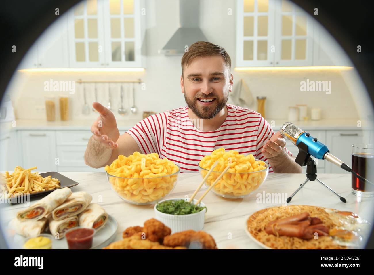 Blogger with lots of food and microphone at table in kitchen, view