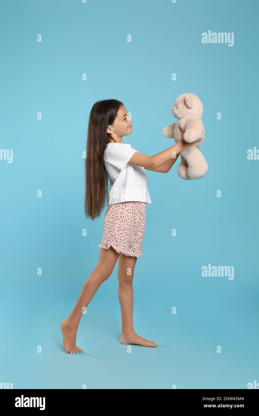 Cute girl wearing pajamas with teddy bear on light blue background ...