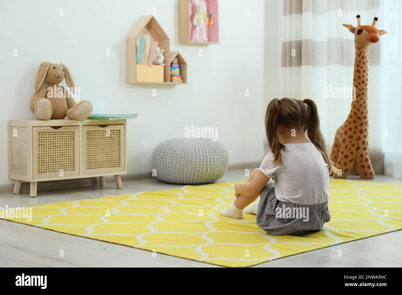 Lonely little girl sitting on floor at home, back view. Autism concept ...