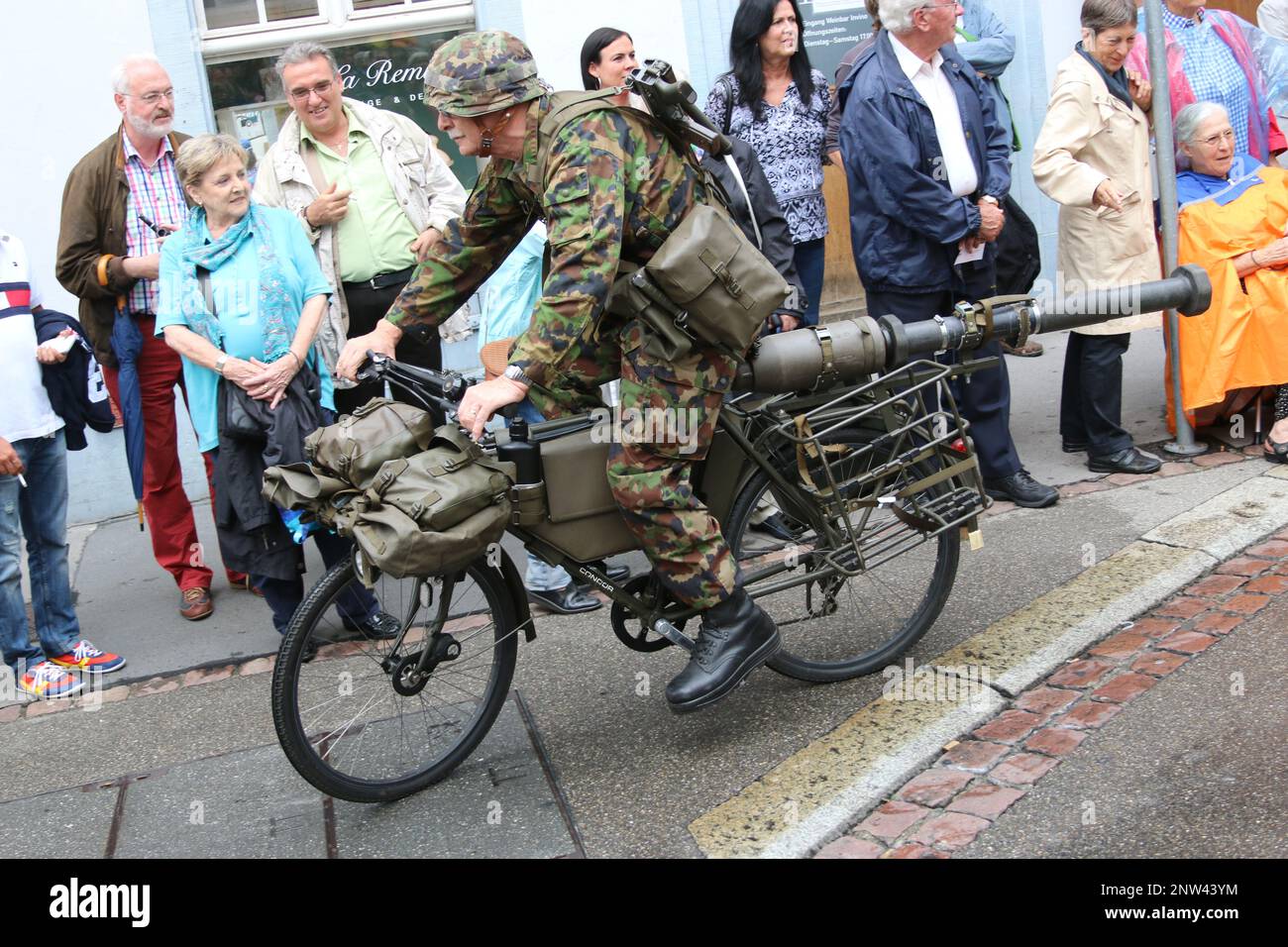 Ein alter Mann transportiert auf einem Fahrrad eine Panzerabwehrwaffe. Gesehen in Basel bei einer Parade. Stock Photo