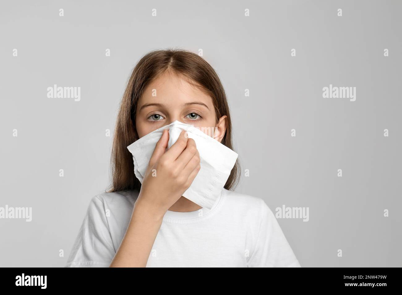 Little girl blowing nose into paper tissue on light grey background