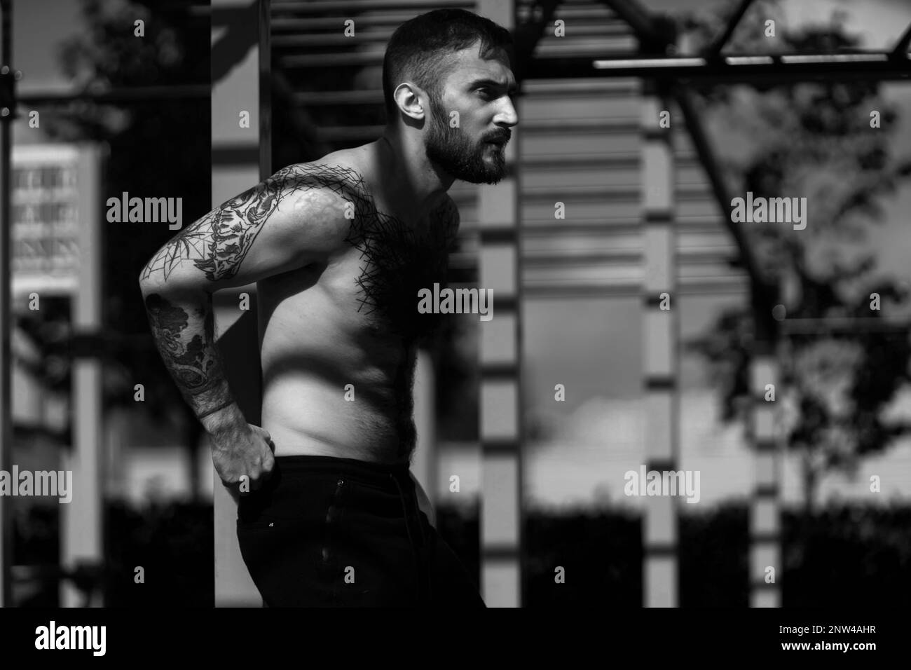 Muscular handsome man is training upper body on machines on street sports ground in city centre. Stock Photo