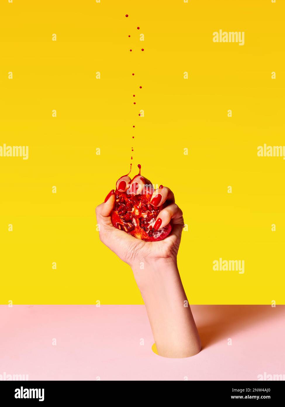 Human hand with red painted nails squeezing half of pomegranate over