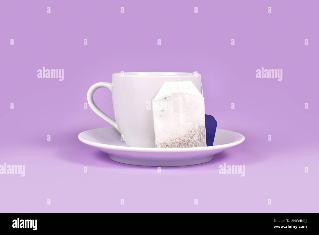 Tea cup with herbal tea bag on violet background Stock Photo