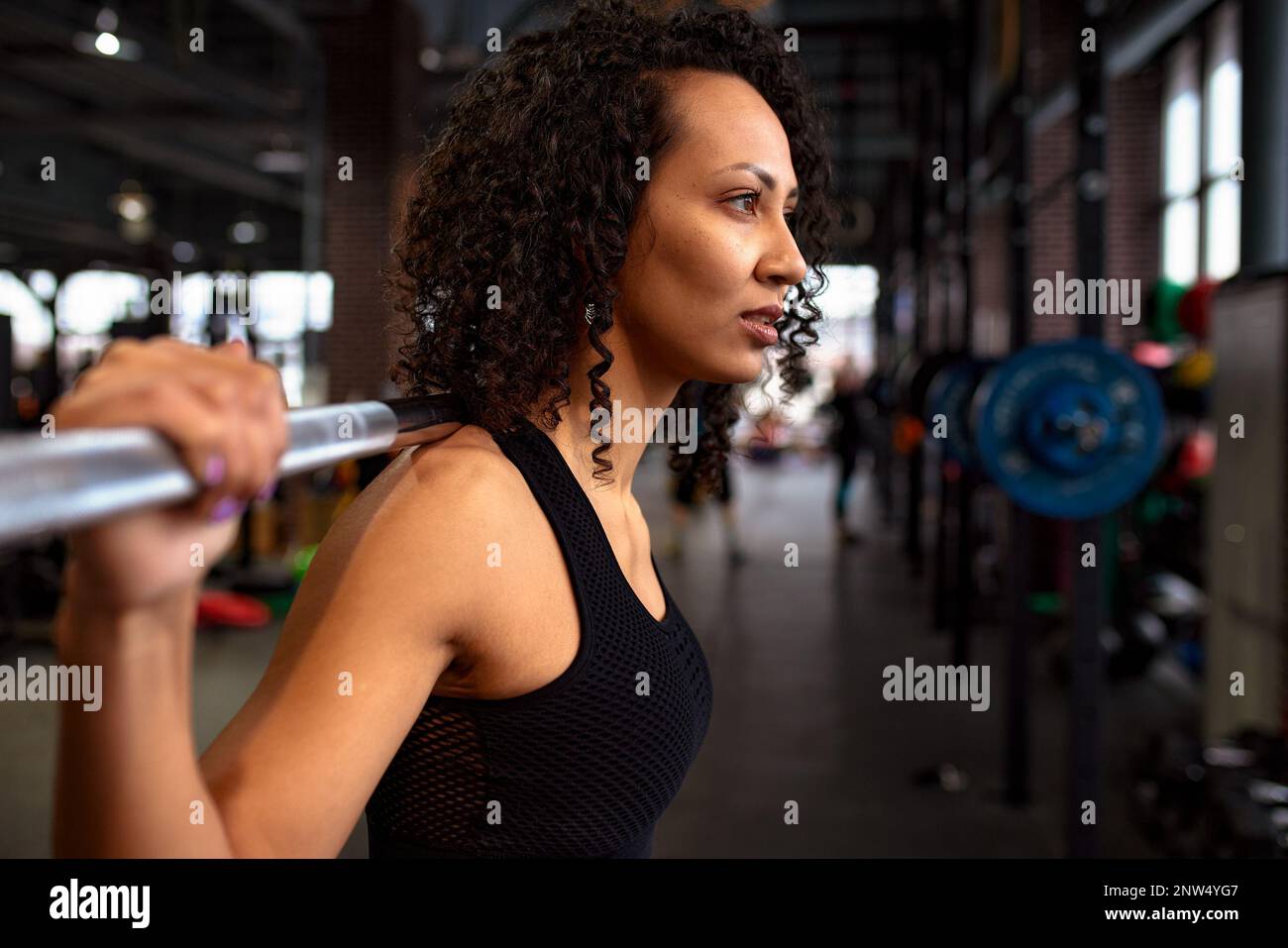 Young pretty african american sports woman in fitness gym lifting up