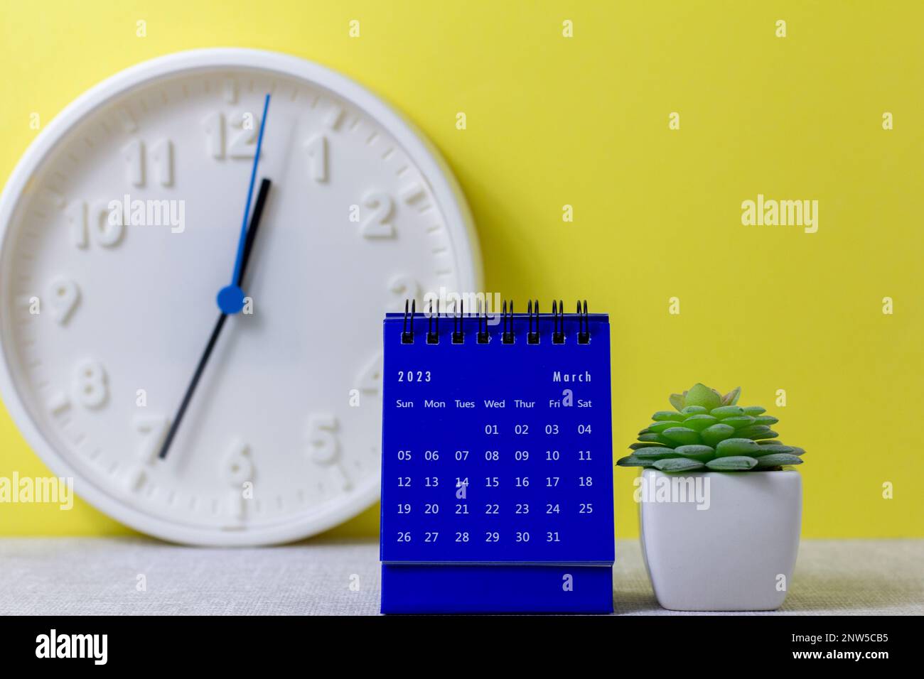 A desktop calendar for March 2023 and a clock on the table for planning