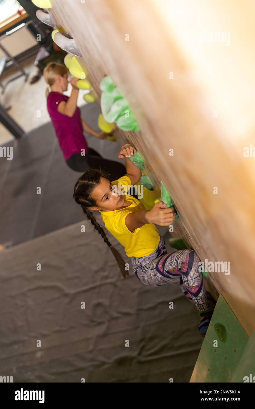 Young female bouldering instructor helping boy climb artificial wall