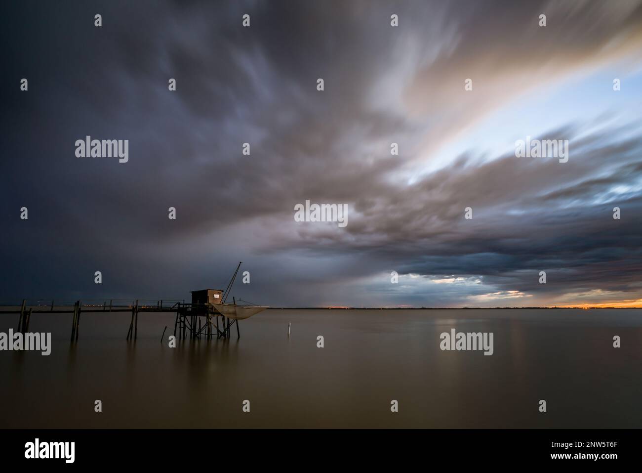 Coastal fishing hut on stilts in calm sea and storm clouds on horizon at sunset Atlantic coast France on Gironde river estuary, Charente Maritime Stock Photo