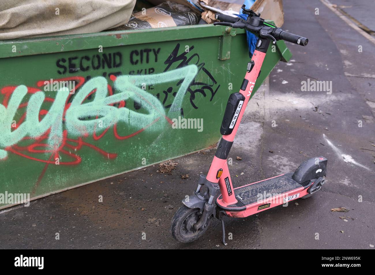 Birmingham, 28th February 2023 - A Voi electric scooter dumped next to a Second City skip in Birmingham - Voi Scooters, the only available hire scooter company in Birmingham will be shutting down their operations on Tuesday 28th February at 11pm. The electric scooters were already thin on the ground in England's Second City after the company said they would be removing the vehicles over the next few weeks. The company ran hire scooters for a trial period but have decided not to continue with the contract and no other company have stepped up to fill the vacancy. Despite calls from local authori Stock Photo