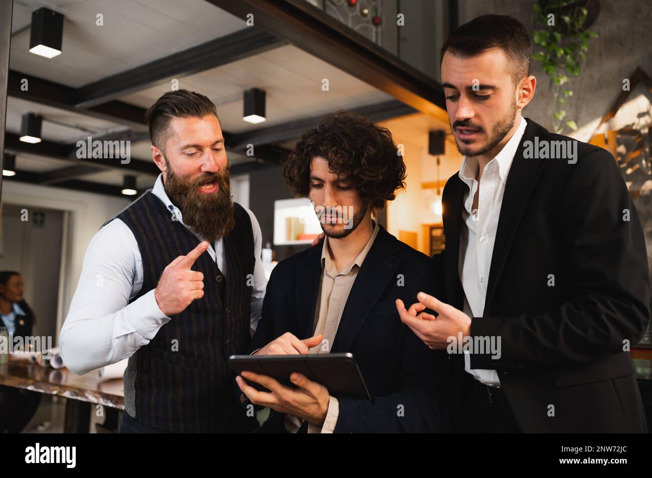 Three young businessmen discussing about something using digital tablet in workplace. Stock Photo