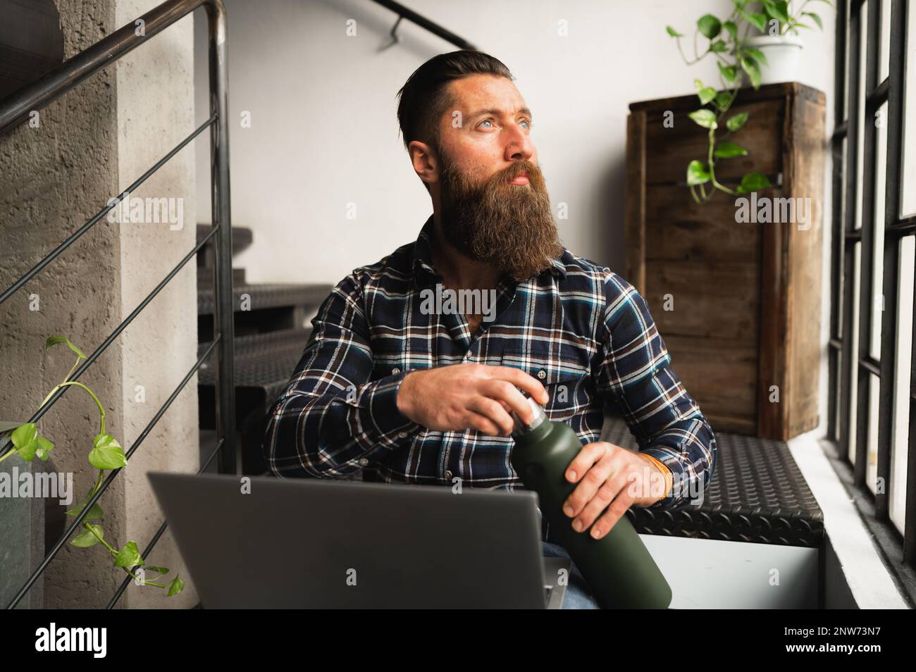 Hipster man looking out window.Guy sitting on stairs using computer. Stock Photo