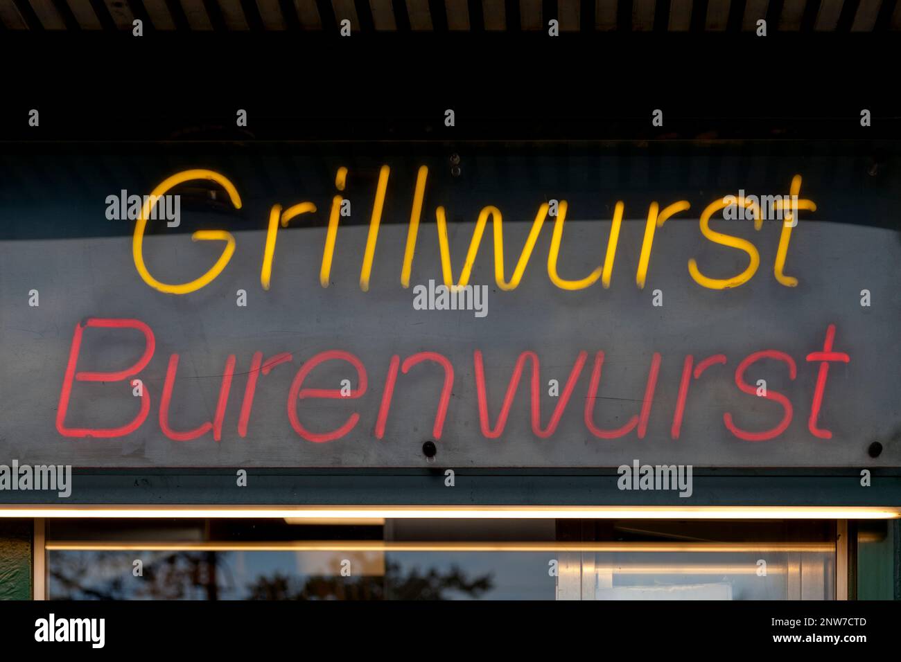 Close-up on a red neon light shaped into the German words 'Grillwurst' and 'Burenwurst'. Stock Photo