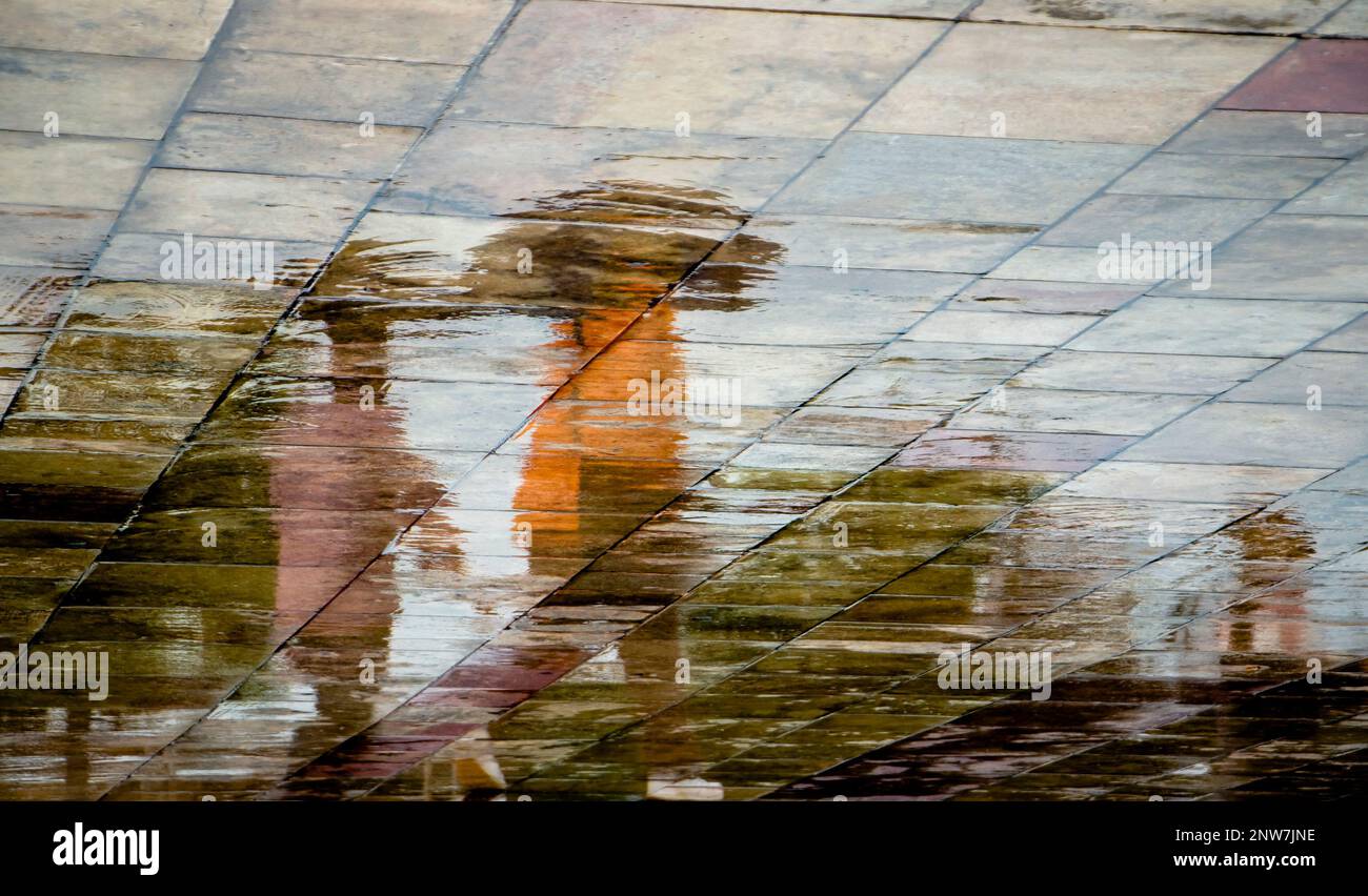 Abstract blurry silhouette shadow reflections of unrecognizable people walking under umbrella on wet city street pavement on a rainy day Stock Photo