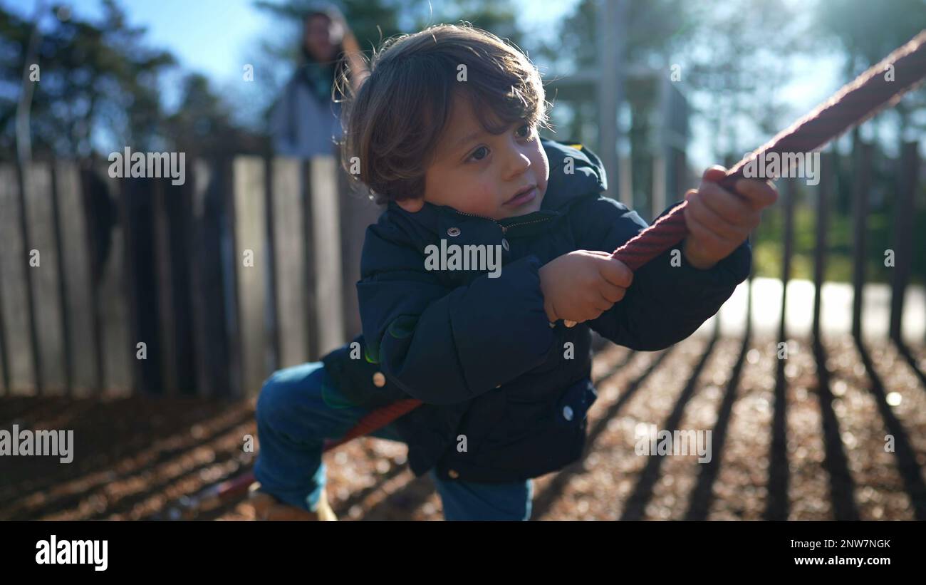 Small boy holding into playground rope during sunny winter season ...