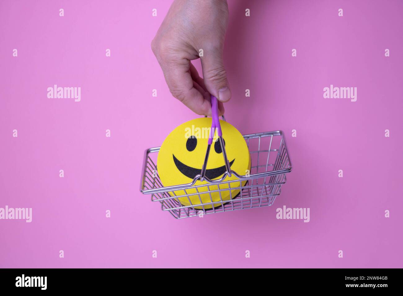 The hand holds a basket with a yellow smiling smiley face on a pink background. Stock Photo