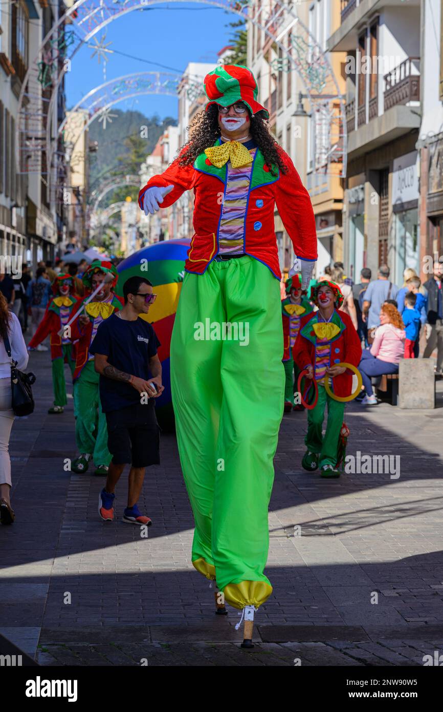A colourful clown stiltwalker leads a procession of clowns through the streets of San Cristobal de la Laguna in Tenerife during the La Noche en Blanco Stock Photo