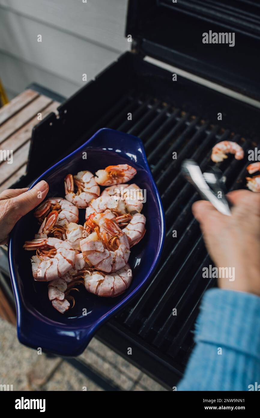 woman using tongs to take Patagonian prawns off barbecue grill Stock Photo