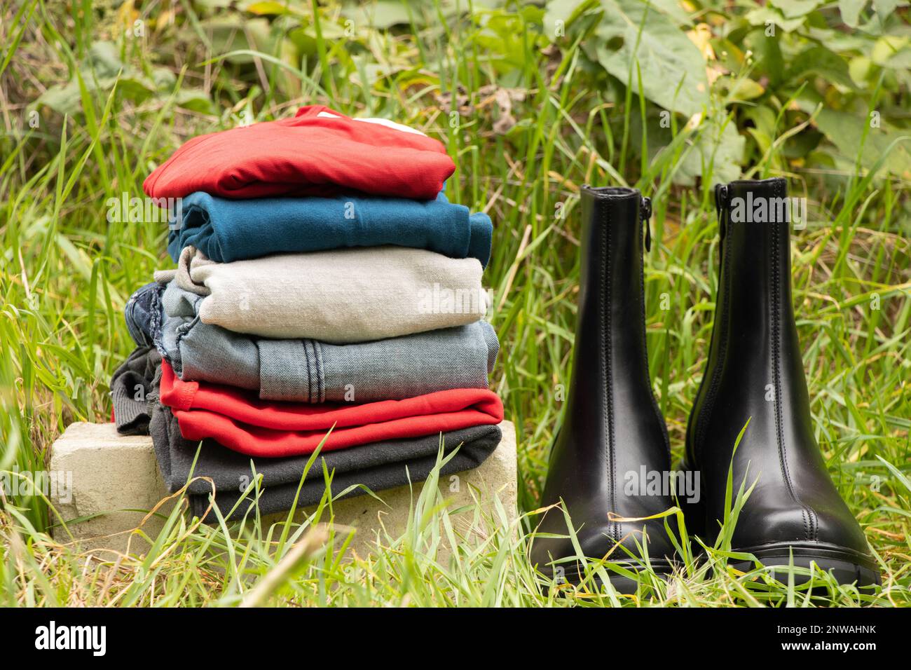 women's high black boots with thick soles and a pile of things stand on the grass in the sun outside, women's shoes and winter clothes, fashionable cl Stock Photo