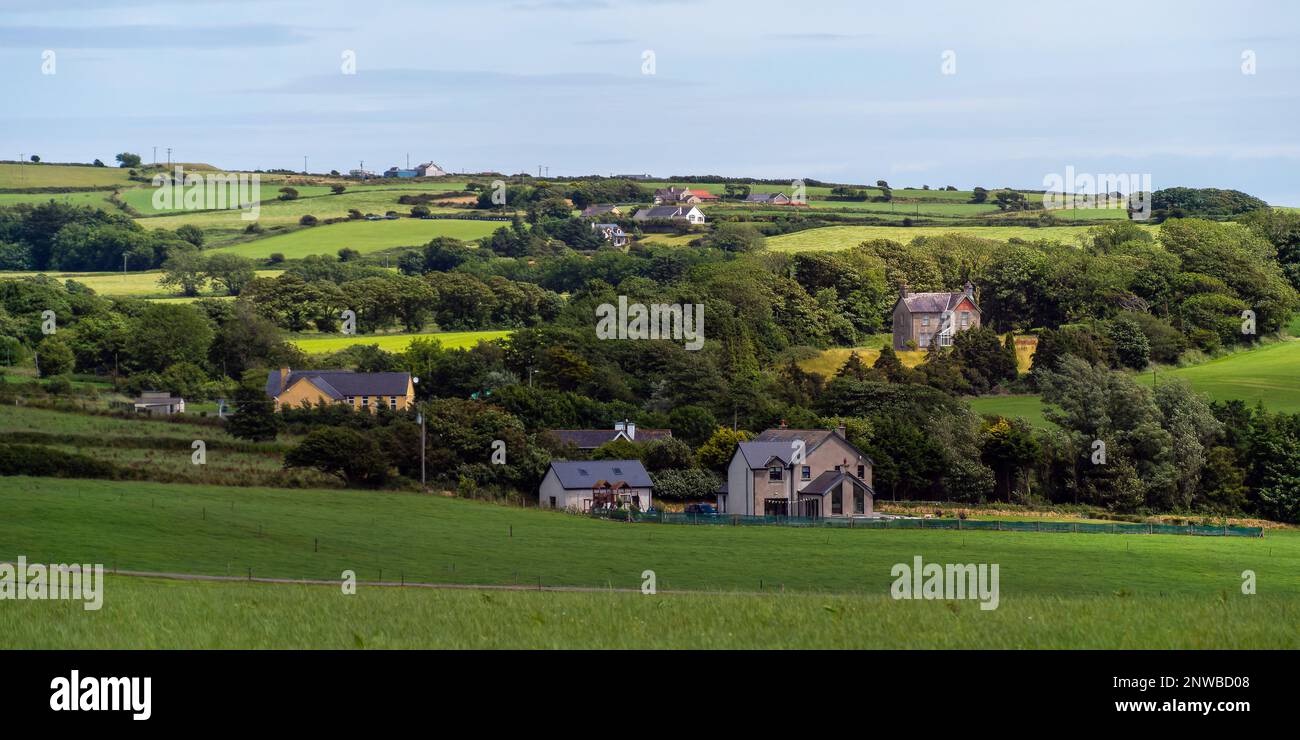 A small European village among green fields and trees. Farmhouses in Ireland. Picturesque agricultural landscape. Green fields under a blue sky, house Stock Photo