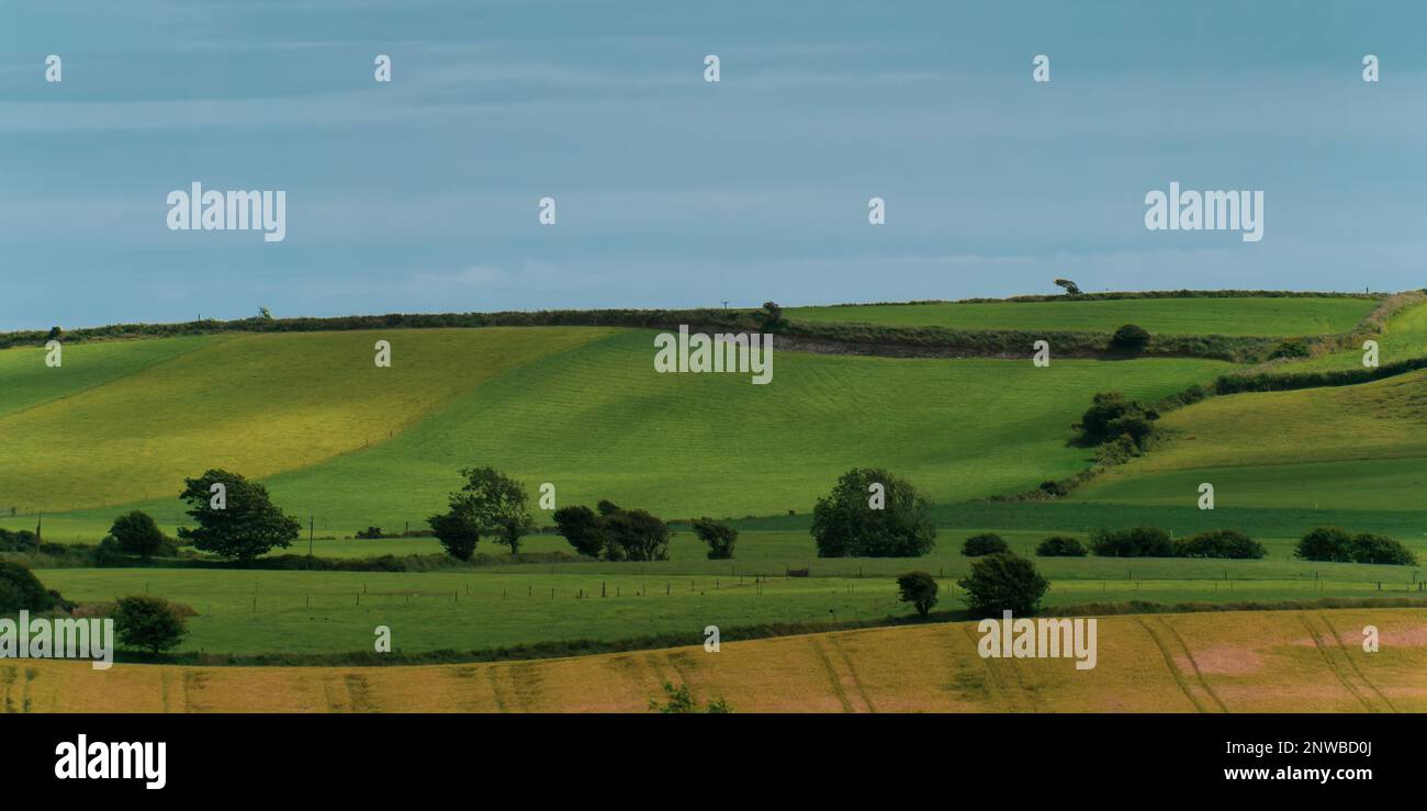 Picturesque agricultural landscape. Green hills under a blue sky. Hilly terrain in the south of Ireland, nature. Stock Photo