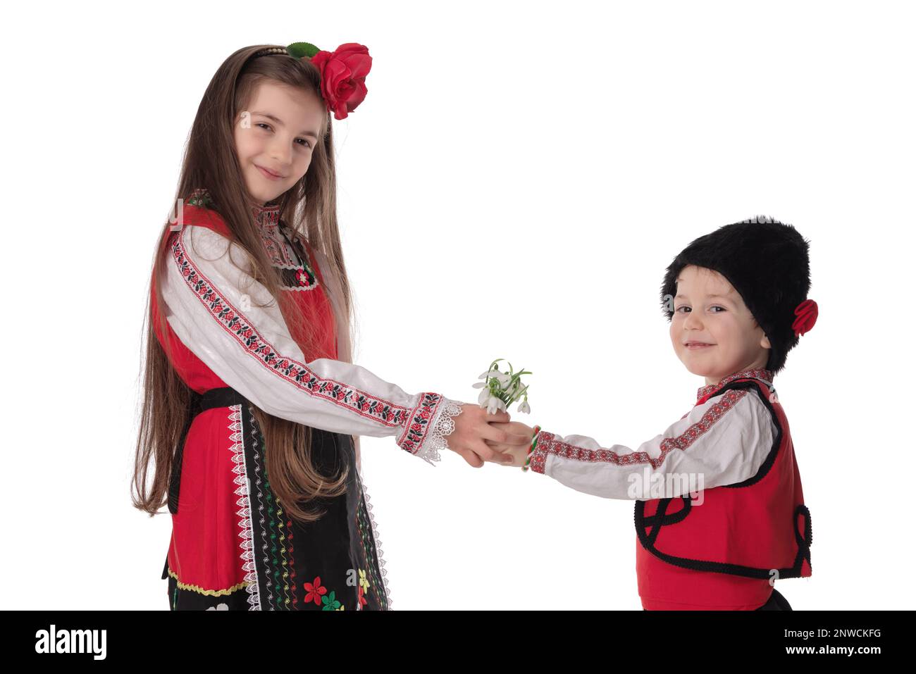 Bulgarian kids boy, girl in folklore ethnic costumes, bouquet spring flowers snowdros, wool martenitsa symbol of March Baba Marta holiday, Bulgaria Stock Photo