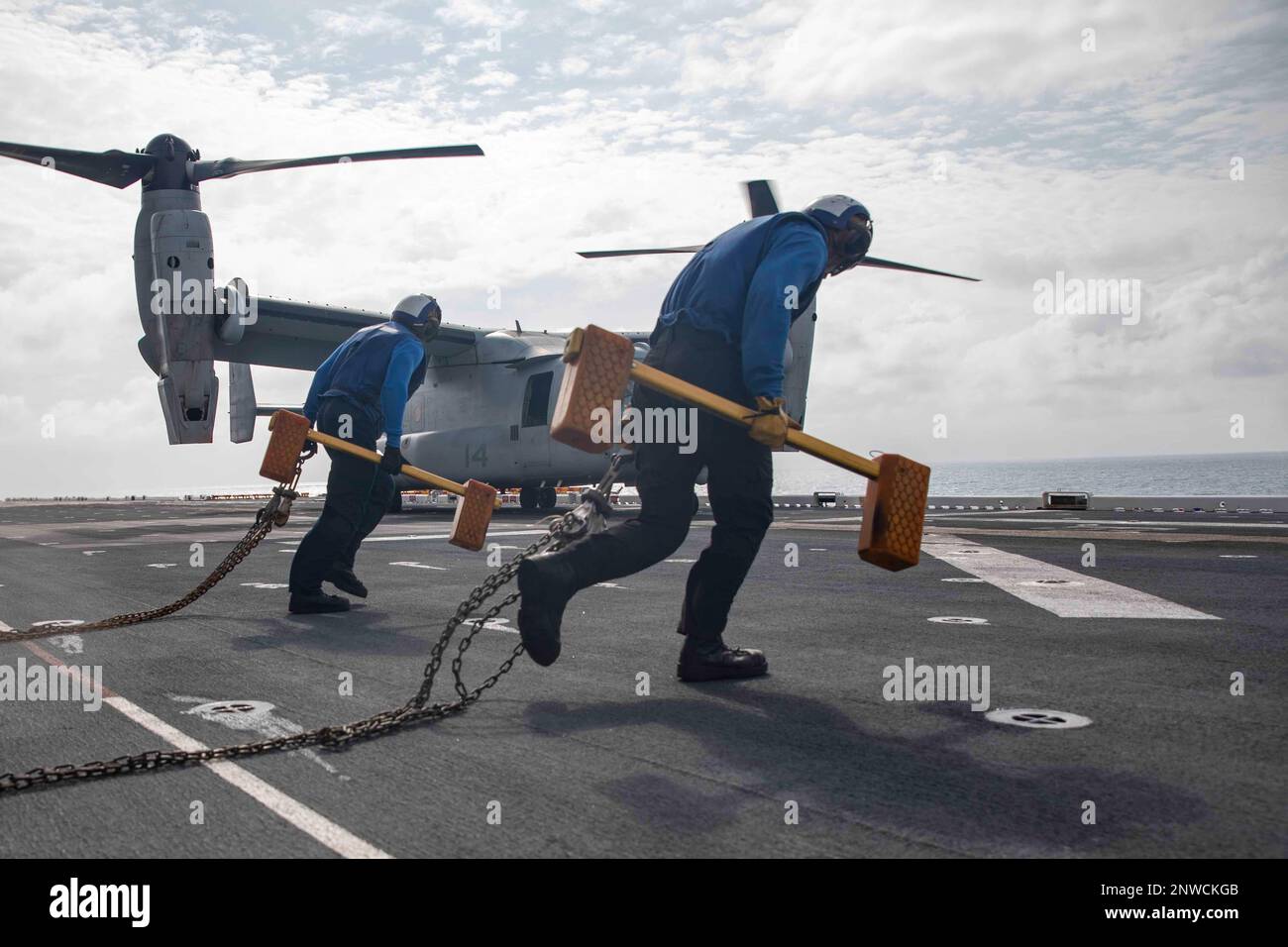 230102-N-VS068-2075    SOUTH CHINA SEA (Jan. 2, 2023) – Aviation Boatswain’s Mate Airman Gabriel Harris, right, and Airman Abdirahman Mohammed carry chocks and chains to an MV-22 Osprey, assigned to Marine Medium Tiltrotor Squadron (VMM) 362 (Rein.), 13th Marine Expeditionary Unit, on the flight deck of amphibious assault ship USS Makin Island (LHD 8), Jan. 2, 2023. Makin Island is designed to field an integrated amphibious force that can support operational commanders around the globe with both strike and amphibious capabilities. The Makin Island Amphibious Ready Group, comprised of amphibiou Stock Photo