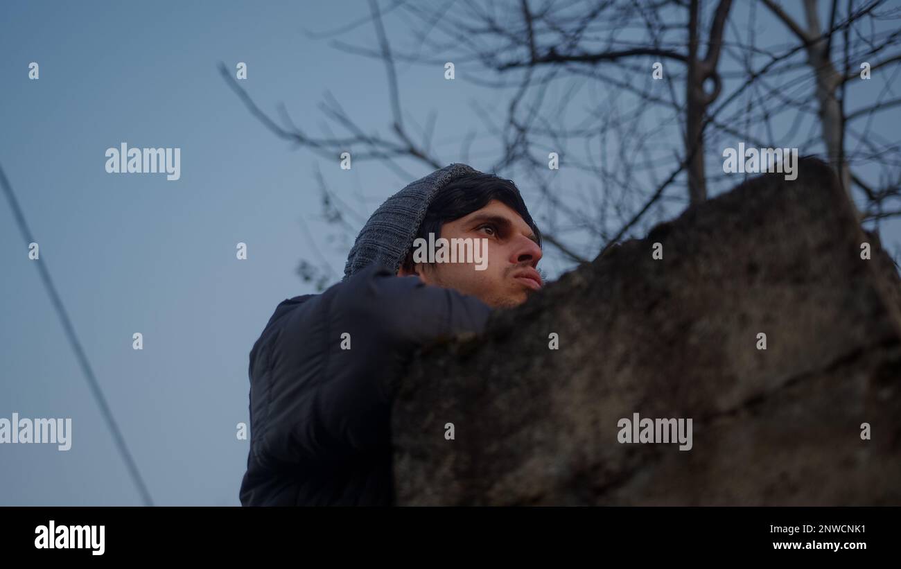Young man in a hat leans against the wall, sighs and looks out at the ...