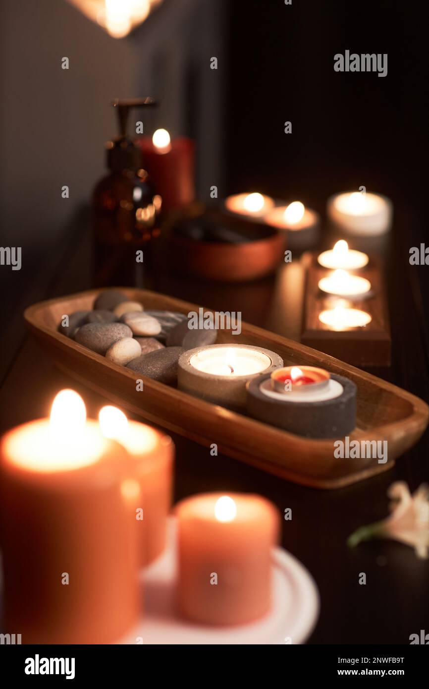 Wooden bowl with stones and burning candles in massage room in spa ...