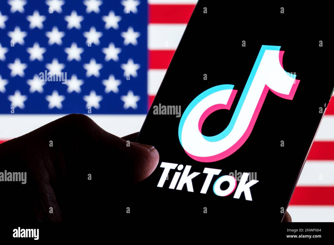 TikTok app logo seen on smartphone screen. U.S. US flag o the blurred background. Stafford, UK, February 28, 2023 Stock Photo