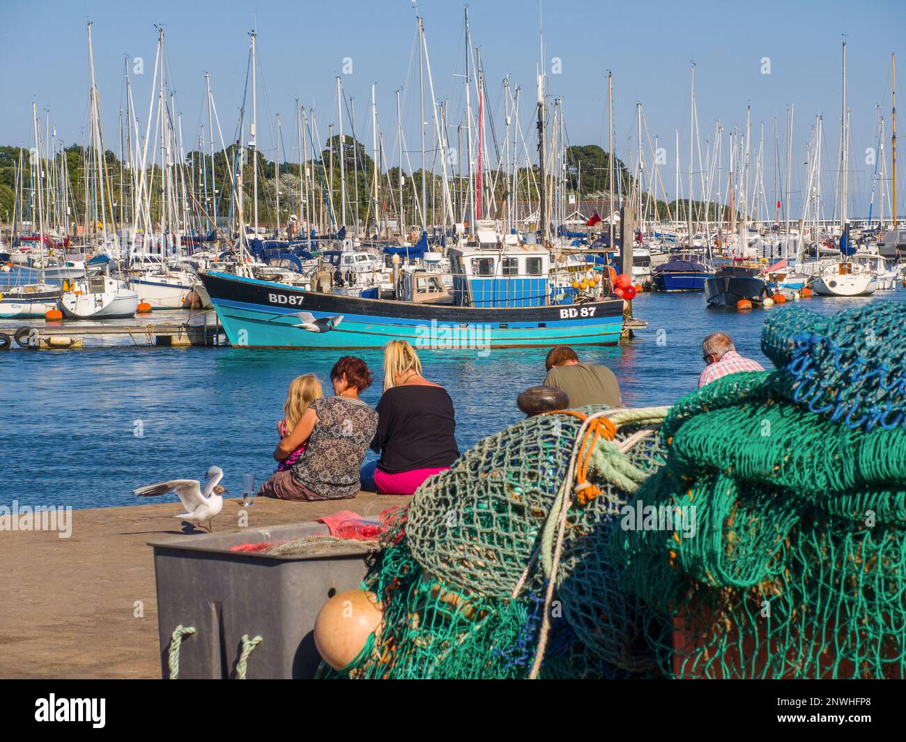 Family sitting on quay at Lymington harbour and marina Stock Photo
