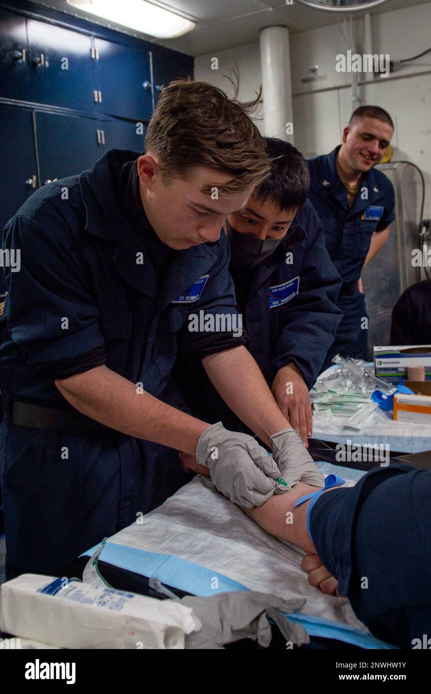 YOKOSUKA, Japan (Jan. 25, 2023) – Seaman Scottie Pennington, from Perris, California, inserts an intravenous needle with training from Hospital Corpsman 1st Class Shuhei Hamaguchi, from Detroit, during a Tactical Combat Casualty Care Course aboard U.S. 7th Fleet’s flagship USS Blue Ridge (LCC 19), Jan. 25. The Combat Lifesaver Course provides Sailors with hands-on training to ensure they are prepared to respond to medical emergencies. Blue Ridge is the oldest operational ship in the Navy and, as 7th Fleet command ship, routinely interacts and operates with Allies and partners in preserving a f Stock Photo