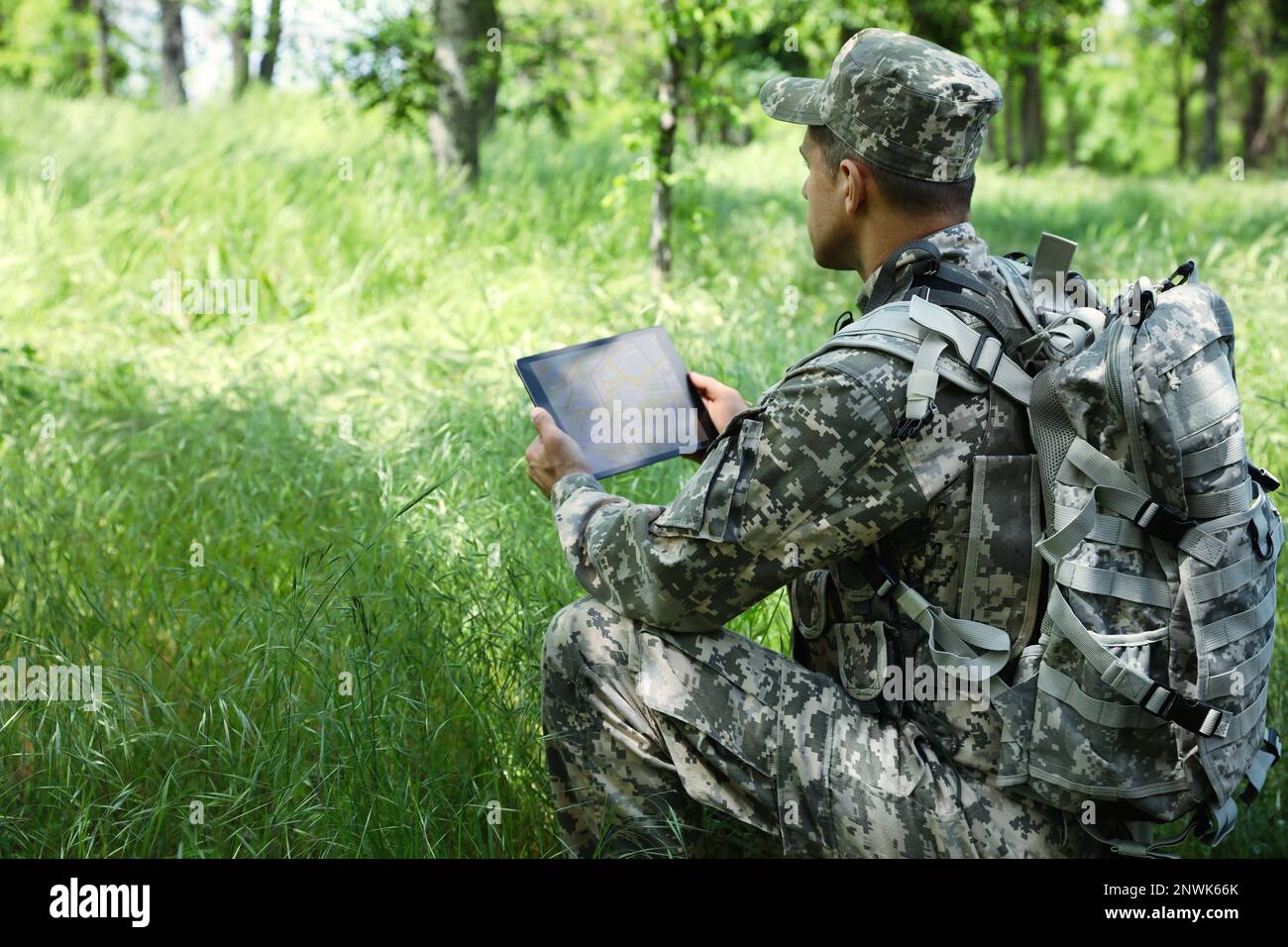 Soldier with backpack using tablet in forest Stock Photo