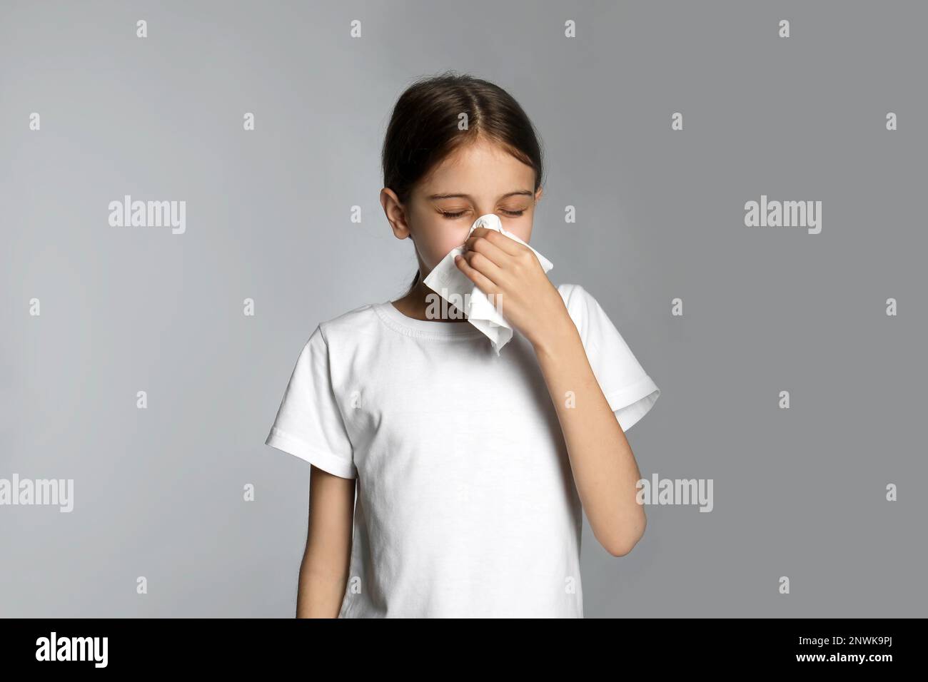 Little girl blowing nose into paper tissue on light grey background