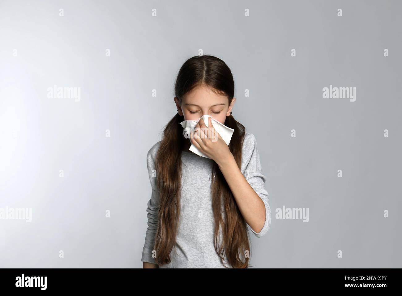 Little girl blowing nose into paper tissue on light grey background