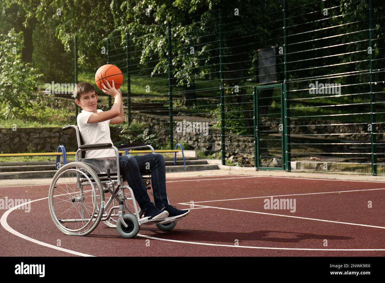 Disabled teenage boy in wheelchair playing basketball  on outdoor court Stock Photo