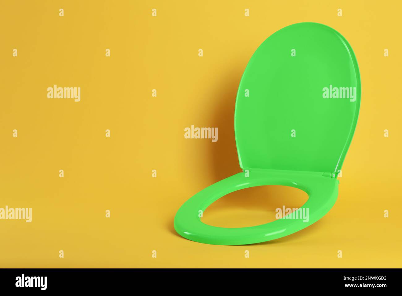 New green plastic toilet seat on yellow background, space for text Stock Photo