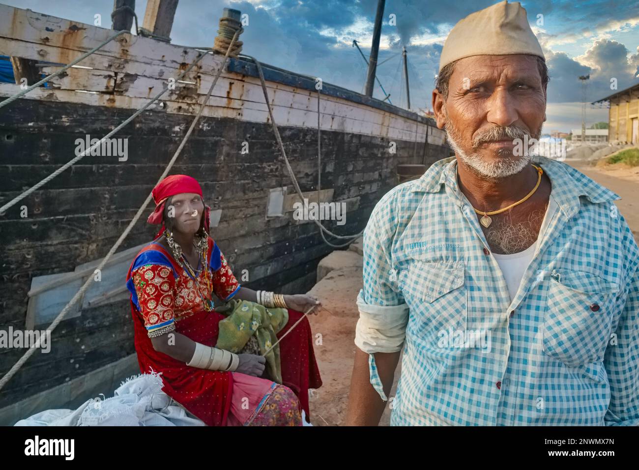 Portrait of an Indian man in the Old Port of Mangalore, Karnataka, India, a colorfully dressed woman from the Lambari (Lambadi) tribe sitting nearby Stock Photo