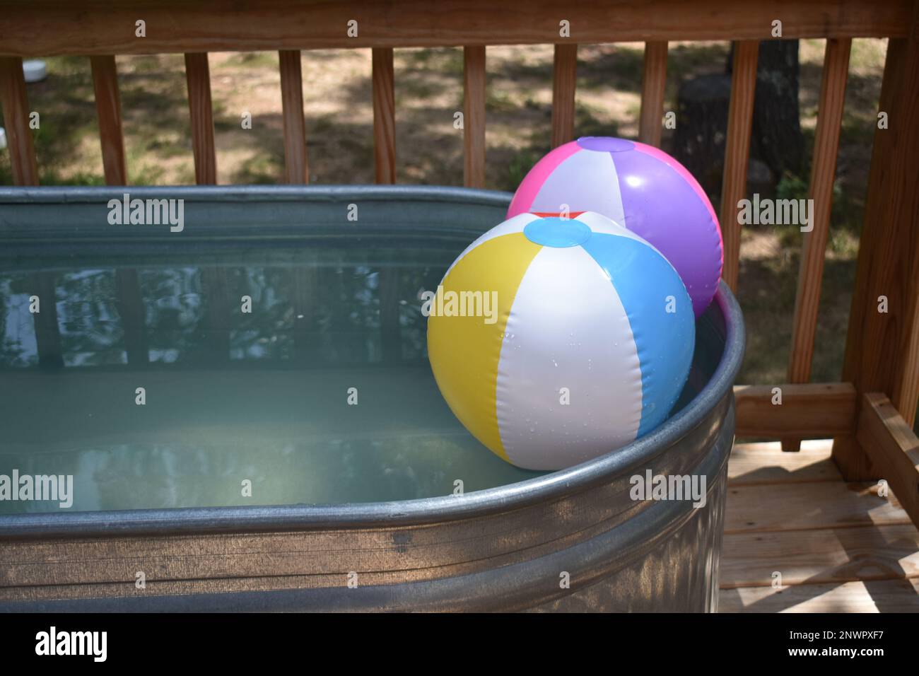 Two inflated beach balls floating in a stock tank pool.  A refreshing place to cool off on a hot summer day. Stock Photo