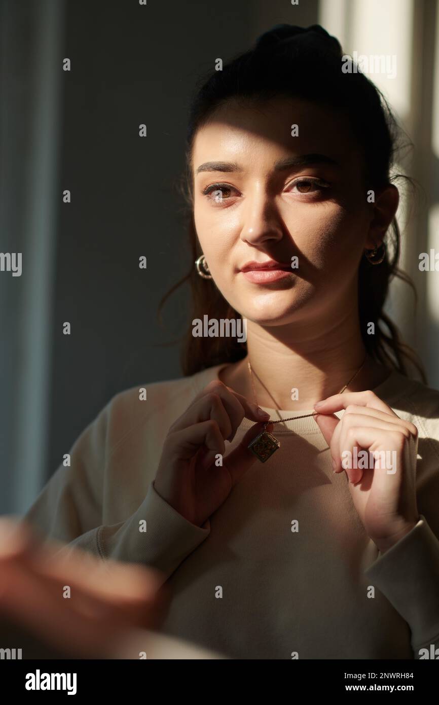 Portrait of serious young woman putting on jewelry Stock Photo