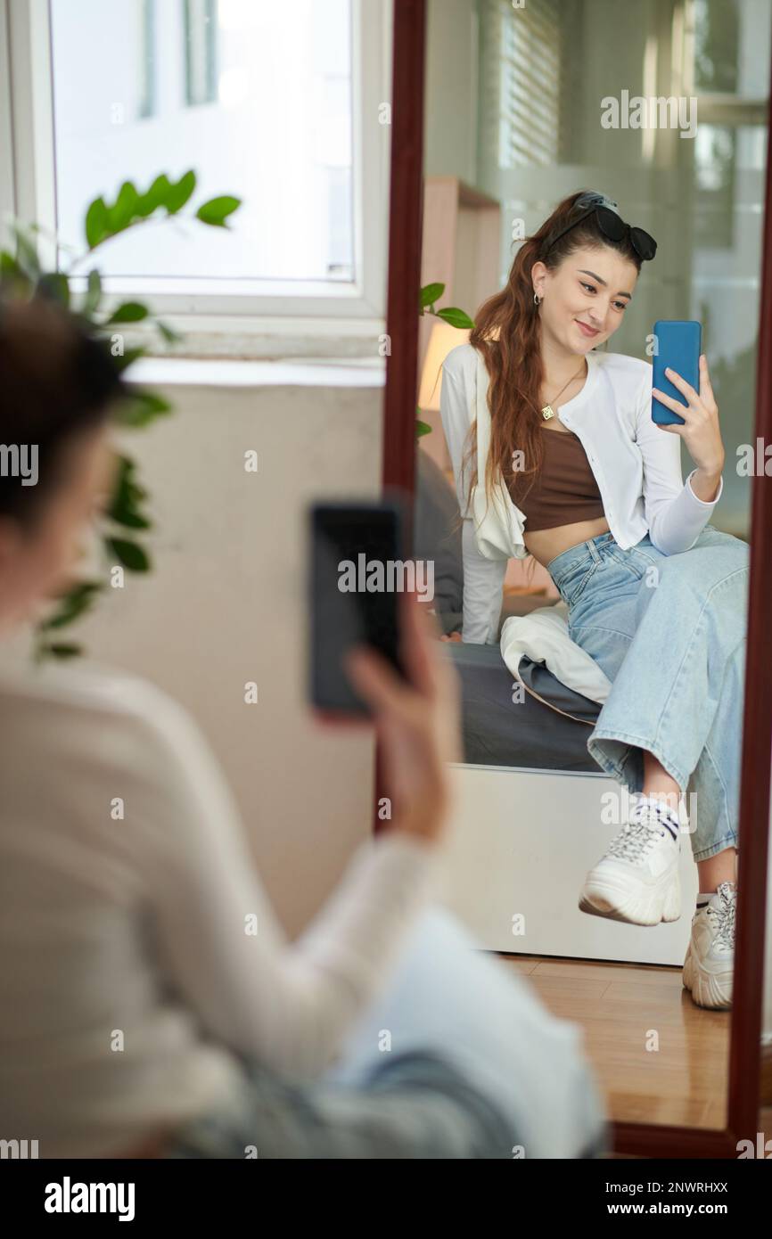 Smiling girl sitting in front of mirror and taking selfie Stock Photo