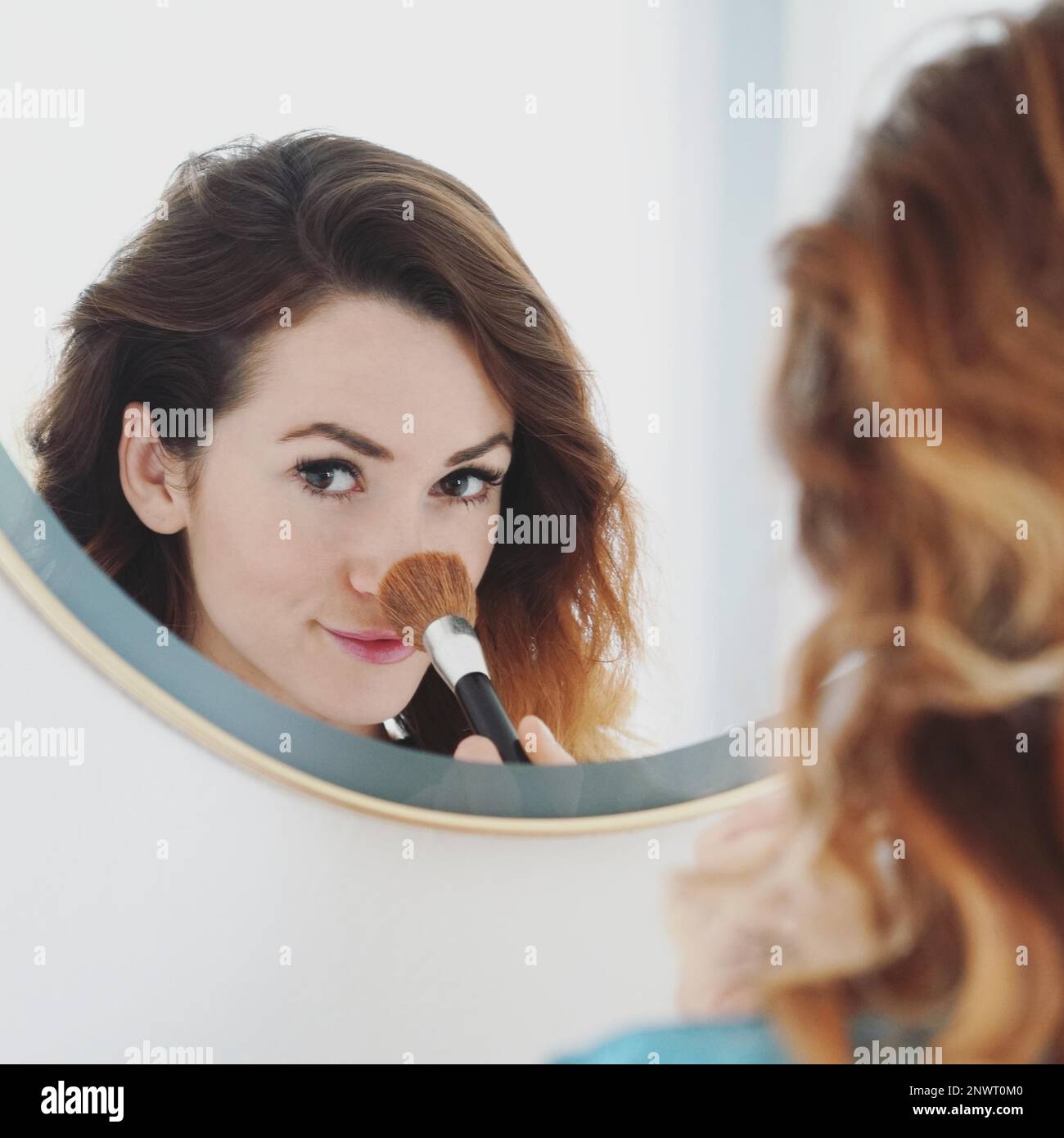 young woman powdering her nose with make-up brush, bathroom mirror, portrait with selective focus Stock Photo
